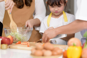 Obraz na płótnie Canvas Asian parents are teaching their daughters to easy home cook salad foods. Family enjoys cooking together home cook in kitchen room at modern home. Focusing on center girl children.