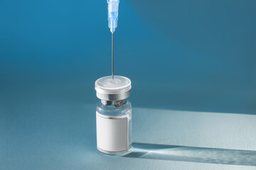 Blue glass vial flask with liquid and syringe on a blue background with hard shadows. The dose of a...