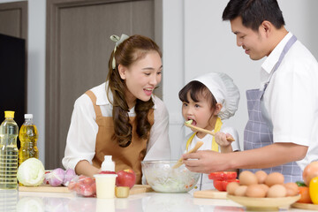 Asian family enjoy cooking together salad foods homemade in kitchen room at modern home. Create activities together in the family. Focusing on center girl children while eating.