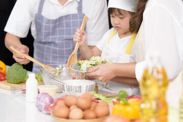 Asian family enjoy cooking together salad foods homemade in kitchen room at modern home. Create activities together in the family. Focusing on Salad foods finished in mom's hand.