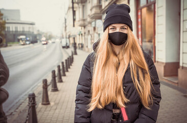 Beautiful girl with long hair in protective mask on city street. Woman in jacket and hat casual style walking in cold weather