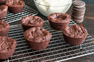 Oreo Stuffed Brownie Cups: Brownie cups filled with a sandwich cookie wire cooling rack with a bowl of frosting in the background