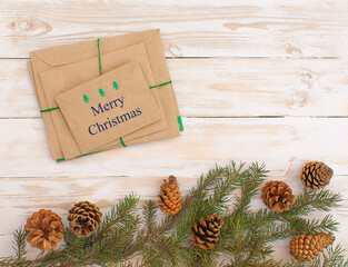 Christmas envelopes with wishes next to fir branches and cones on white wood background