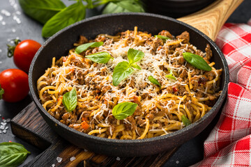 Pasta Bolognese, Spaghetti with meat ragout in tomato sauce in the skillet at black table. Italian cuisine.