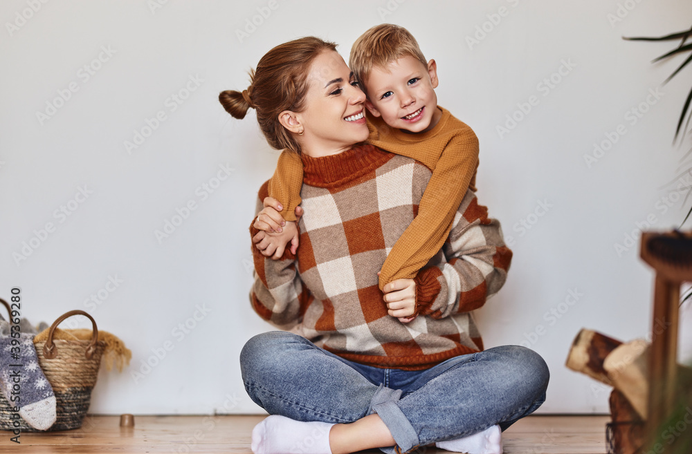 Sticker happy family mother and loving son in warm sweaters hug and laugh sitting on floor near wall at home