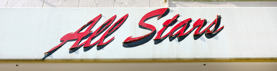 Weathered, peeling ALL STARS sign mounted on exterior building wall.