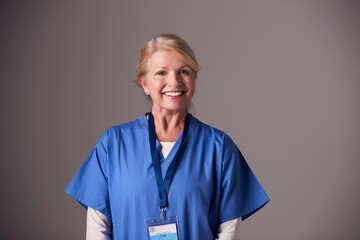 Studio Portrait Of Mature Female Nurse Wearing Scrubs Standing Against Grey Background