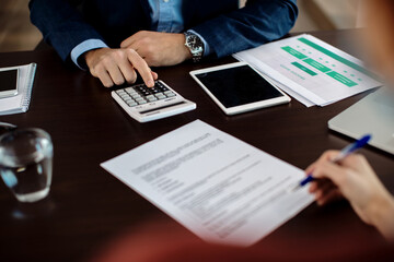 Close-up of real estate agent using calculator while his client is signing a contract