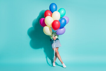 Fototapeta na wymiar Photo of young lady hold bunch balloons cover herself wear green sweater mini jeans skirt sneakers isolated blue color background