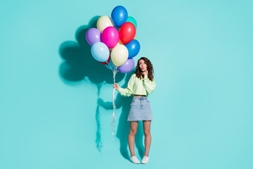 Photo of girl hold many balloons finger cheek look empty space wear green sweater mini jeans skirt sneakers isolated blue color background