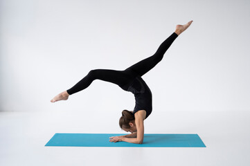 Young woman is practicing yoga in a studio. Slim young girl in a black sport wear is doing yoga practice on a blue mat. Concept of healthy life and natural balance between body and mental development.