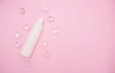 White plastic bottle for shampoo or other cosmetics. Ice cubes around, pink background, free space for text, top view.