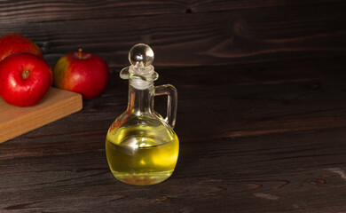 Apple cider vinegar in a glass decanter on a dark wooden table. Apples nearby. Free space.