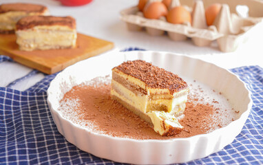 Delicious Tiramisu - traditional italian dessert from mascarpone cheese and biscuit. gourmet tiramisu dessert topped with chocolate powder served on a white plate at table background.