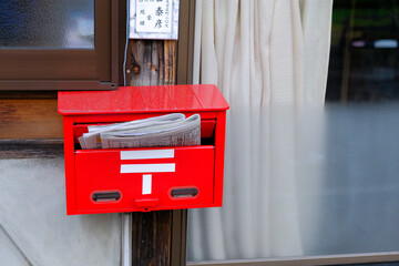 closed up the japanese red mailbox, Many japan newspapers are hanging from old post box in front house.