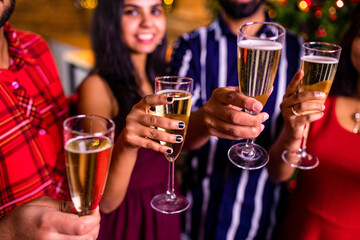 group of four indian friends cheering with champagne flutes and looking happy while having party on the kitchen at stay home quarantine corona virus outbreak party