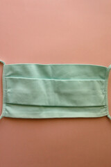 Reusable protective face mask in mint green color. Top view, pink background.