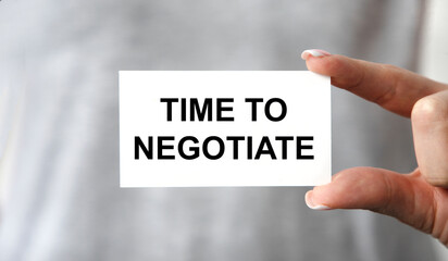 Holds a business card in front of him with the text TIME TO NEGOTIATE, business concept.