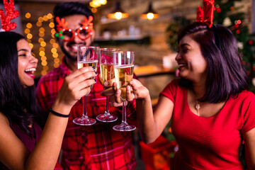 group of four indian friends cheering with champagne flutes and looking happy while having party on the kitchen at stay home quarantine corona virus outbreak party