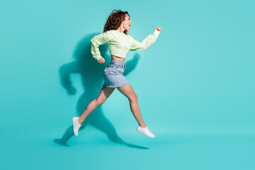 Fototapeta na wymiar Full length body size side profile photo of beautiful girl jumping high hurrying up isolated on vibrant teal color background
