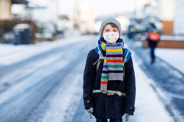 Little kid boy with glasses wearing medical mask on the way to school. Child backpack satchel. Schoolkid on winter day with warm clothes. Lockdown and quarantine time during corona pandemic disease