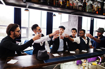 Cheers! Group of handsome retro well-dressed man gangsters spend time at club. Drinking whiskey at bar counter. Multiethnic male bachelor mafia party in restaurant. - obrazy, fototapety, plakaty