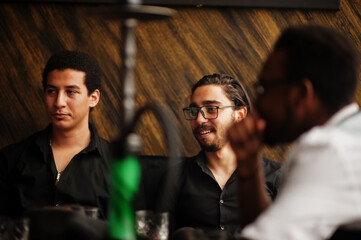 Group of handsome retro well-dressed man gangsters spend time at club, smoking hookah. Multiethnic male bachelor mafia party in restaurant.