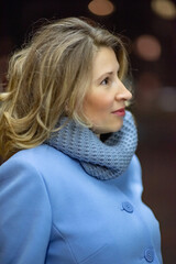 Portrait of a young beautiful blonde woman in a blue coat in the evening city.