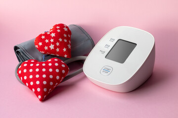 Automatic blood pressure monitor and two soft red hearts on pink background. Medical electronic...
