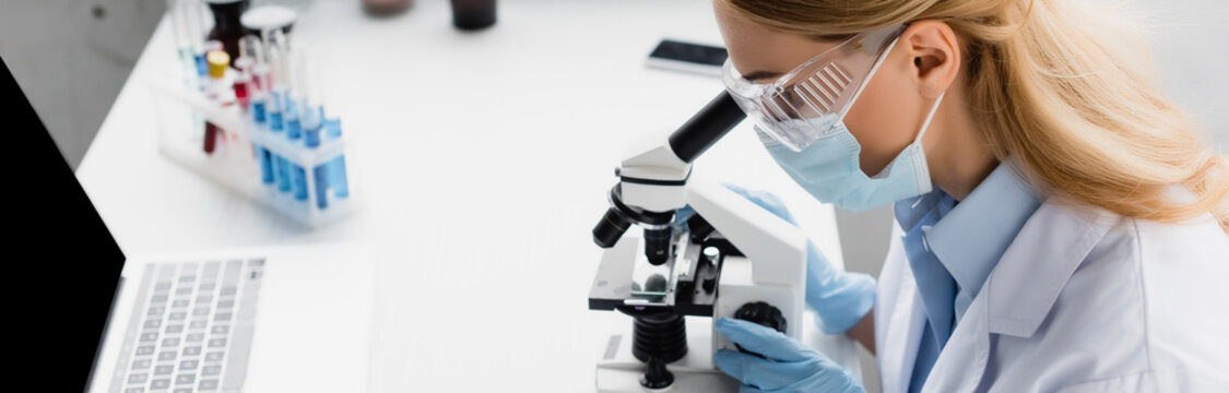 scientist in mask looking through microscope on desk, banner