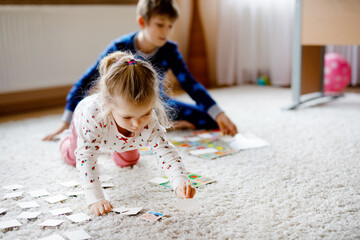 Two little chilren, cute toddler girl and school kid boy playing together card game by decorated...