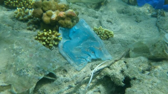 Close-up of used face mask and oter plastic garbage lies on seabed of the Red Sea. Pollution of the coral reef. Plastic pollution of the Ocean. Camera zooming
