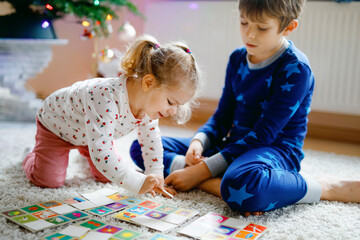 Two little chilren, cute toddler girl and school kid boy playing together card game by decorated...
