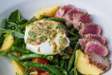 Warm salad with tuna, poached egg, cherry tomatoes, spinach, green beans on plate. Fresh food close-up
