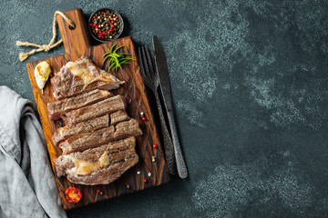 Closeup ready to eat steak ribeye breeds of black Angus with herbs, garlic and butter on a wooden Board. The finished dish for dinner on a dark stone background. Top view with copy space
