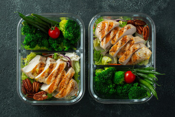 Healthy meal prep containers with green beans, chicken breast and broccoli. A set of food for keto diet in lunchbox on a dark concrete background. Top view