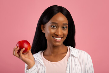 Portrait of happy black woman with tasty red apple on pink studio background, panorama