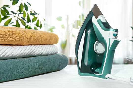 Home work concept: green clothes iron and towels on Ironing Board indoors. Activities at home Ironing and folding towels