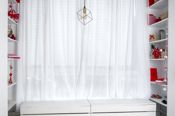 A window with white curtains and shelves on the sides that hold Christmas gifts.