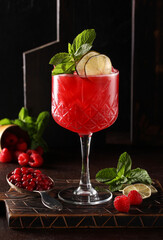 Alcoholic cocktail.Passion berry.Red drink of vodka, raspberries, lemon juice, cranberries and passion fruit and mint in a clear glass on a wooden board on a brown table. Background image, vertical