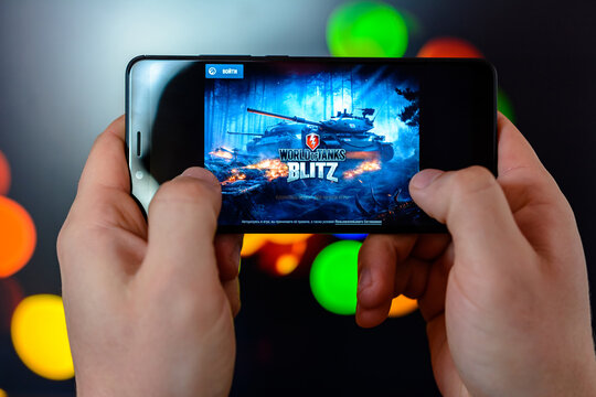Los Angeles, California, USA - 9 March 2019: The man holds the smartphone close-up in his hands and plays the world of tanks blitz against the background of a colored blurred side.