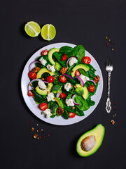 vegetable salad of spinach, avocado, broccoli, cream cheese, cherry tomatoes, walnuts, red onions, dressed with lime juice. Dish on a white plate on a black background, studio shot, flat lay