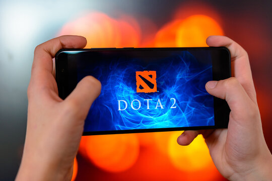 Los Angeles, California, USA - 9 March 2019: The man holds the smartphone close-up in his hands and plays the dota 2 against the background of a colored blurred side.