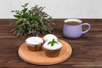 Cupcakes with black currants on a background of flowers and mint leaves, on a round board on a wooden background.
