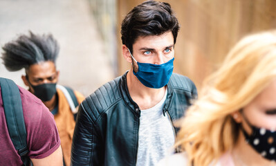 Multiracial crowd walking on city street - New normal lifestyle and society concept about young people citizens with face covered by protective mask - Selective focus on guy with blue eyes