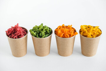 Multicolored pasta in a disposable kraft paper cups on a white background. Copy, empty space for text