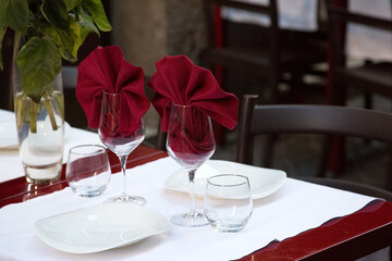 Restaurant table served outdoors for a couple. Two wine glasses with red napkins inside. Art of catering. New year red and white table setting. Nobody. Empty restaurant in pandemic period