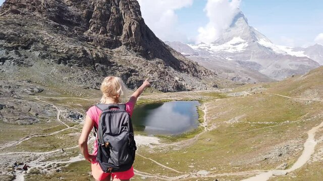 Hiker woman backpacker pointing Mount Matterhorn or Monte Cervino or Mont Cervin, and Swiss Alps and Riffelsee Lake. Activity outdoor in Zermatt, Canton of Valais, Switzerland, Europe.