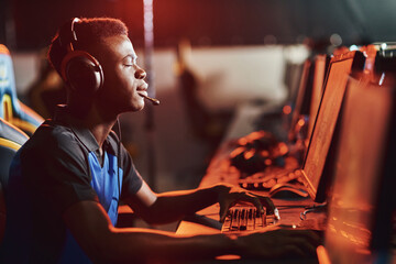 Wishing to win. Side view of a young african guy, male professional gamer wearing headphones keeping eyes closed while playing online video game - obrazy, fototapety, plakaty