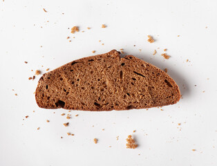 Slice of brown bread with crumbs on white background. Flat lay.